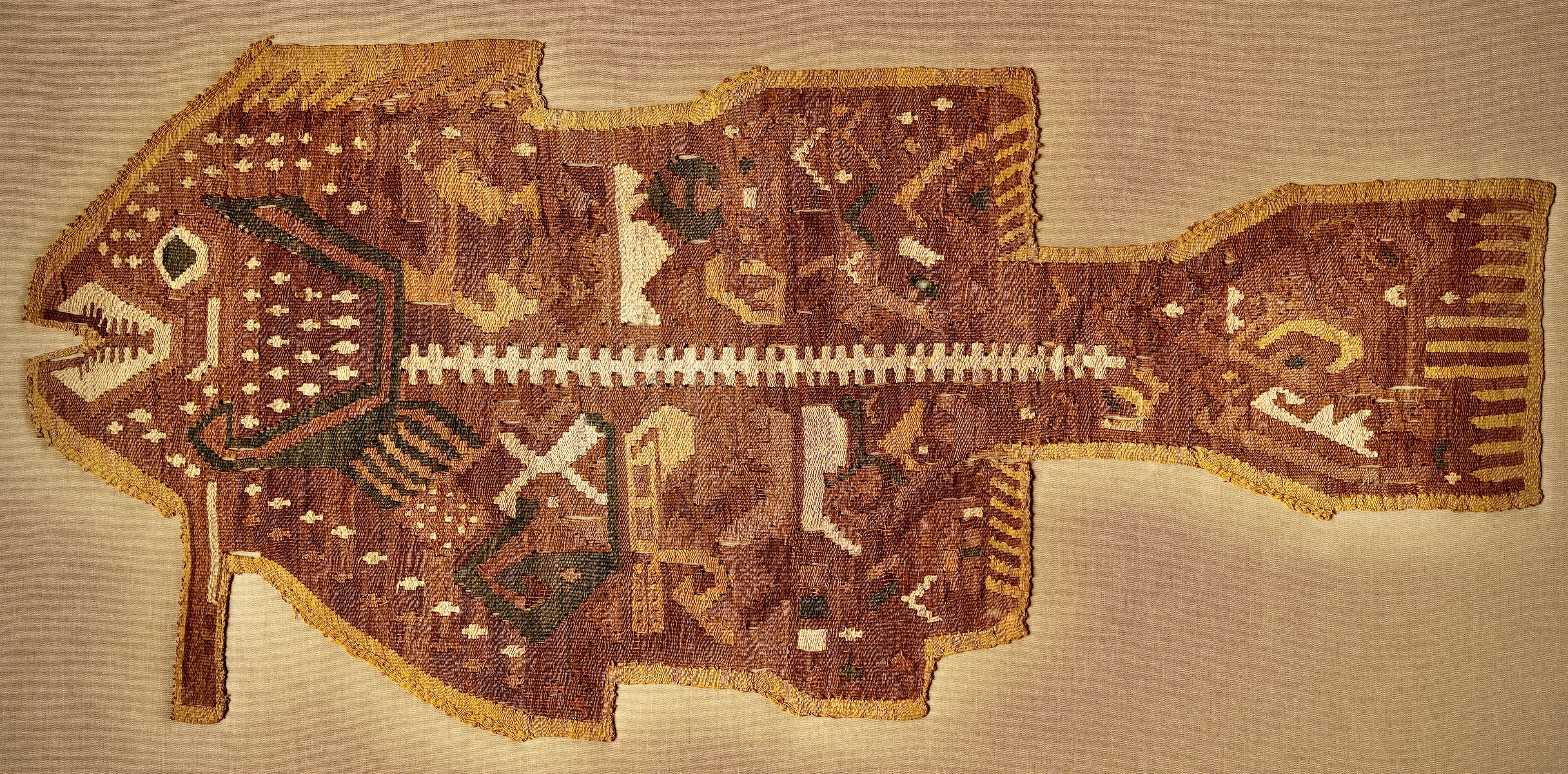 This fish-shaped textile, a complete weaving with 33 finished edges, was stitched with others like it to a mantle, a shawl-like garment that was a staple of ancient Andean wardrobe. The partial “x-ray view,” which emphasizes the bony white teeth and spine, is unique to the style of the Ychsma (yeach-mah), who lived on Peru’s central coast. Marine imagery may relate to both subsistence and religious concerns—at least some coastal people of the period conceived of the sea as a deity.