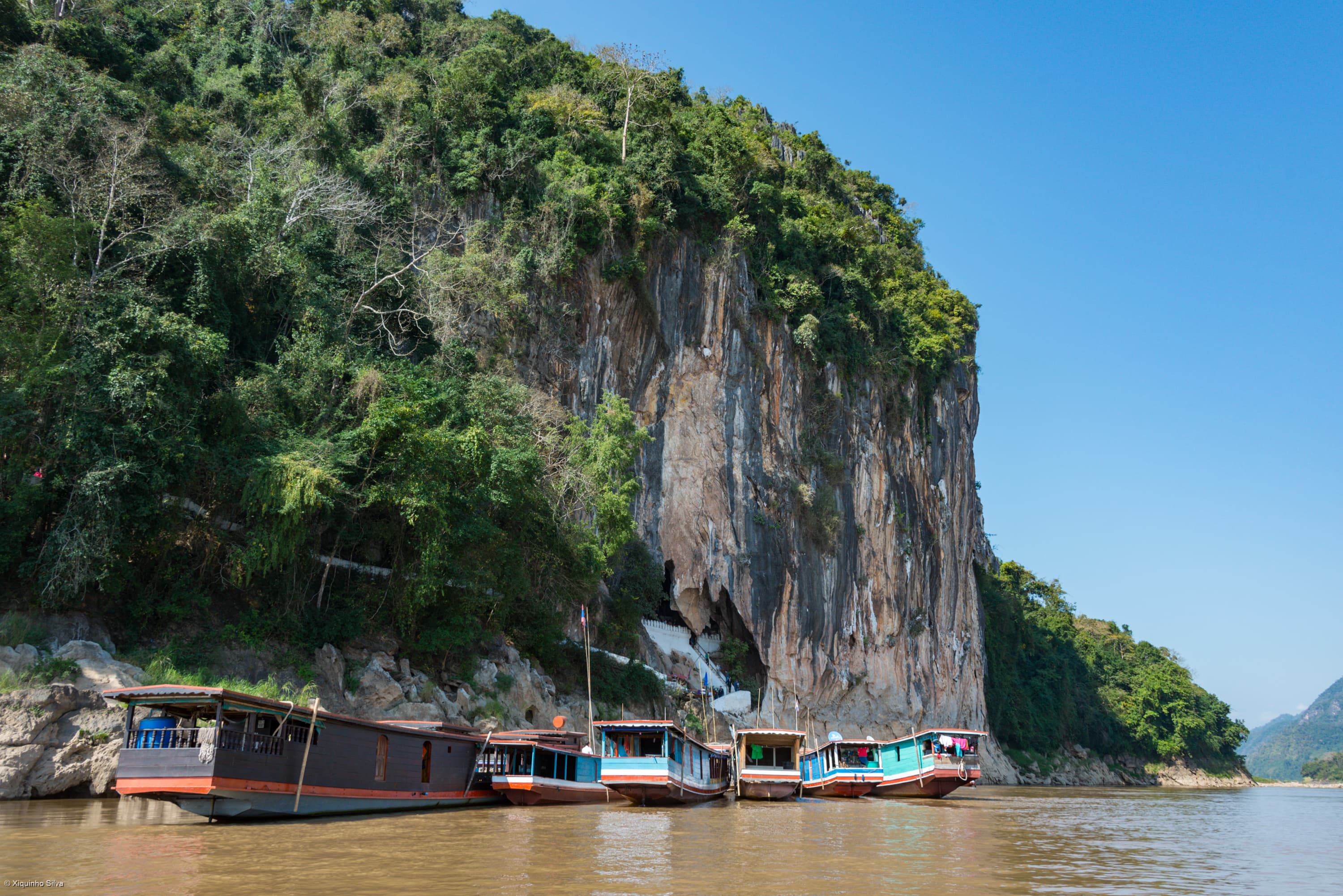 Boats beside the cliff and cave approach at Pak Ou